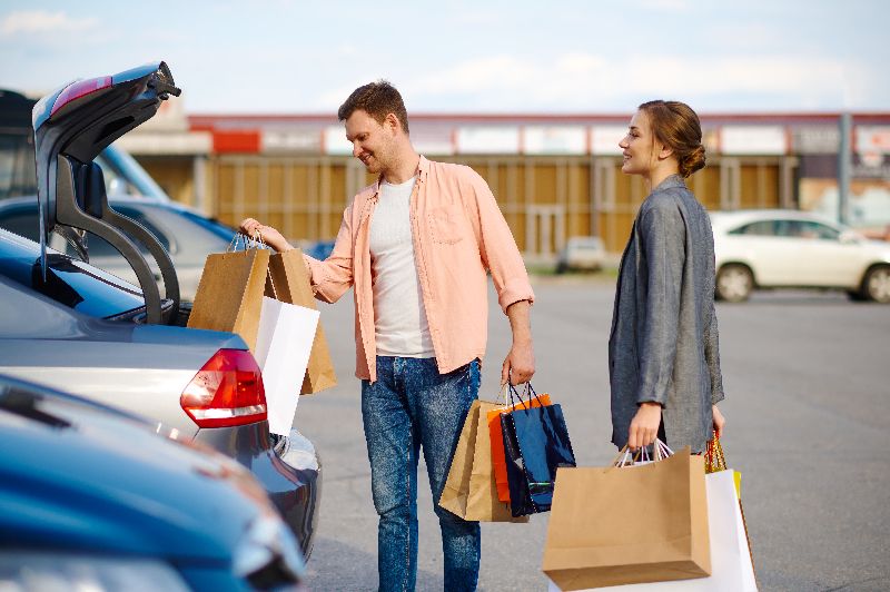 Coppia con uomo che carica shopping bag in auto parcheggiata